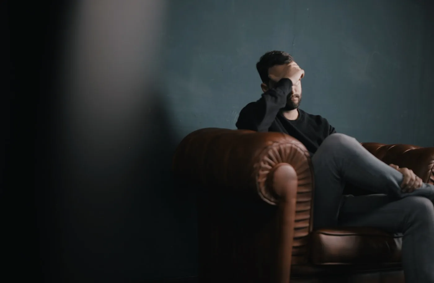 Person sitting on a sofa with a hand on the forehead, evoking fatigue and chronic pain.